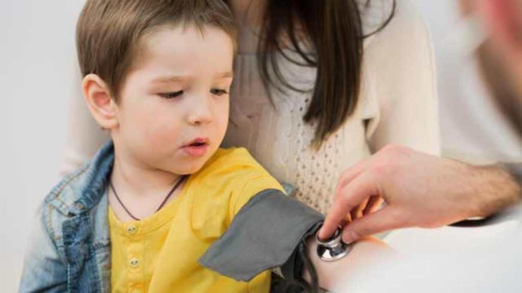 Küçük bir çocuk, doktor muayenesinde kolundan tansiyon ölçülürken