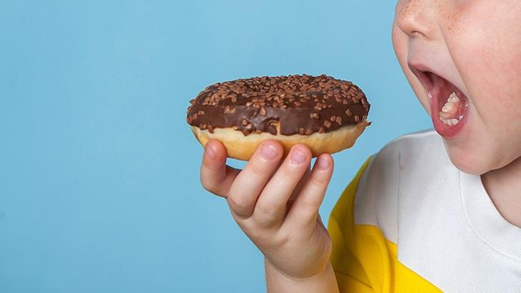 Bir çocuk, çikolata kaplı bir donut yemeye hazırlanıyor
