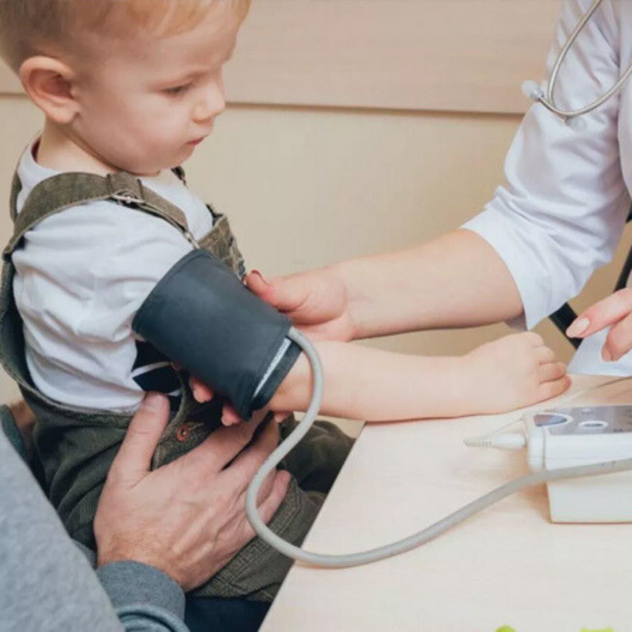 ir sağlık çalışanı, küçük bir çocuğun koluna tansiyon ölçüm manşonunu takarak ölçüm yapıyor.